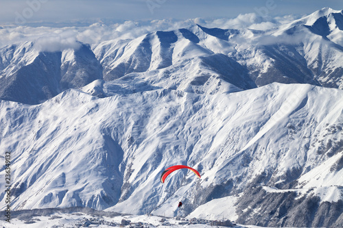 Paragliding at snowy mountains over ski resort at sunny winter day