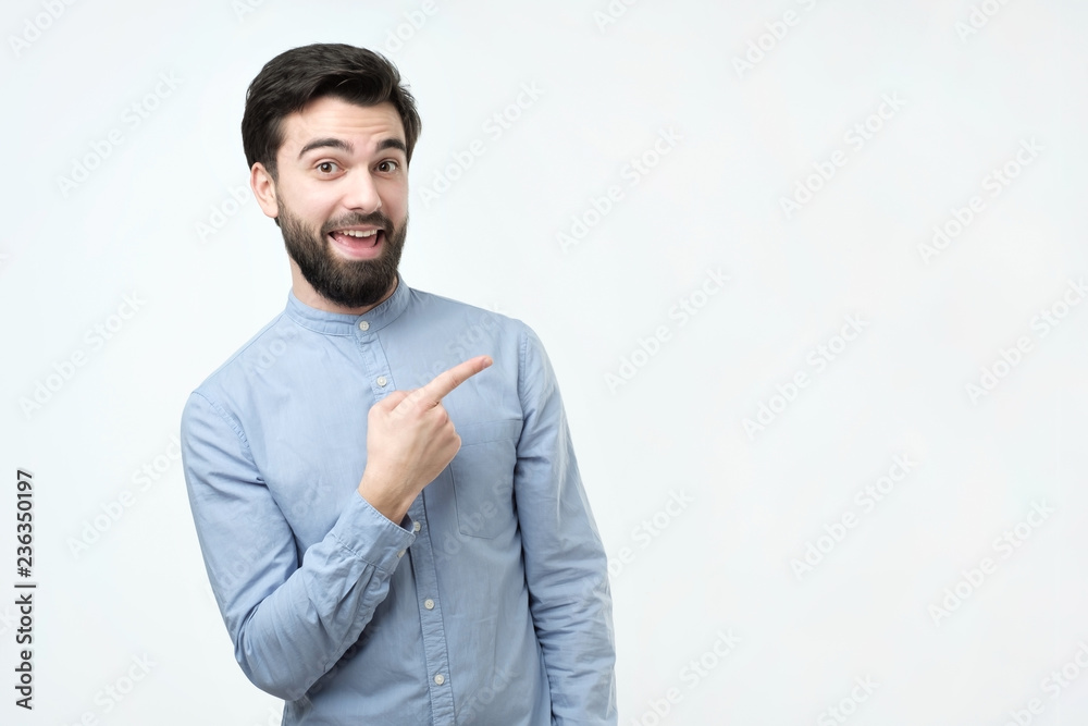 Happy beautiful bearded hispanic man looking at camera, smiling and pointing aside with hand. Pay attention to important information concept Happy beautiful bearded hispanic man looking at camera, smiling and pointing aside with hand. Pay attention to important information concept
