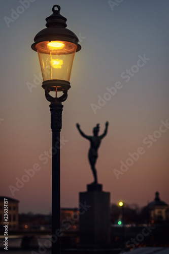 Photography Lit lamp with a statue of the Sunsinger by Carl Milles embracing Stockholm at St