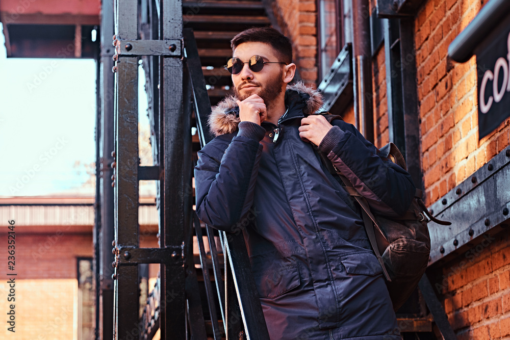 A pensive young man with a backpack standing on stairs outside.