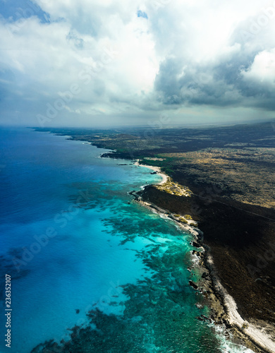 Beautiful Aerial View of Tropical Island Paradise Nature Scene of Big Island Hawaii On Clear Sunshine Blue Sky Day with Vibrant Blue Ocean Water and Waves and Lush Green Mountain Scenic Landscape 