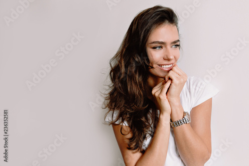Incredible young stylish female student with curly dark hair and big green eyes smiling with great smile wearing white shirt and looking at window with romantic look