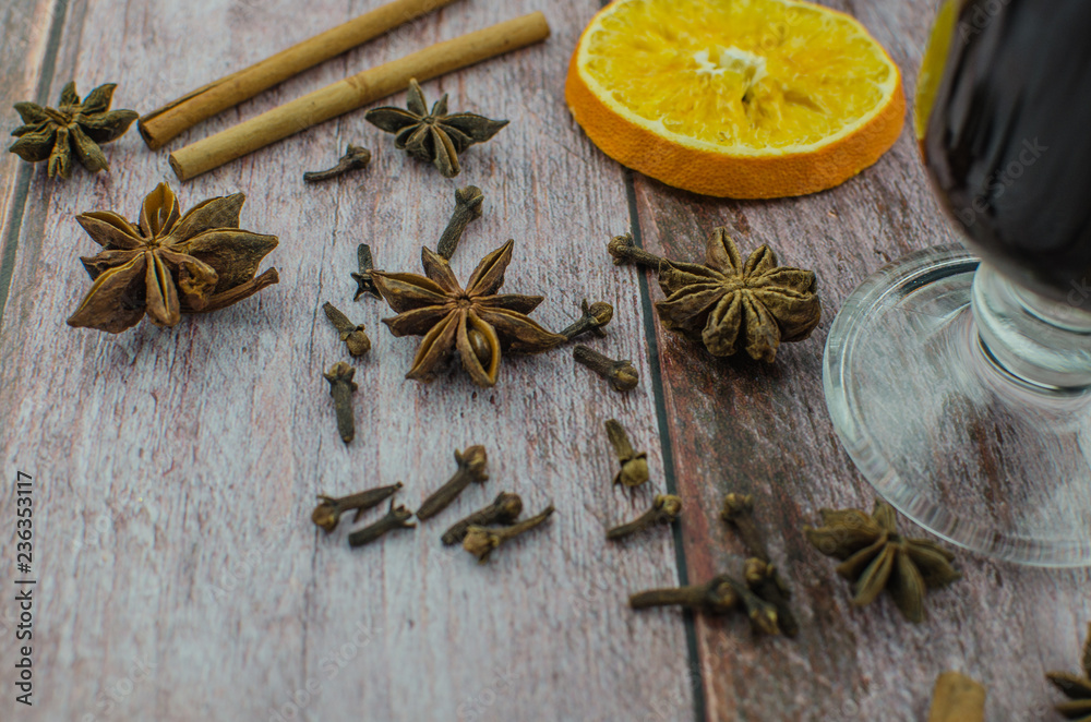 Hot mulled wine drink with lemon, apple, cinnamon, anise and other spices in a glass cup between fir tree branches on wooden cutting board Hot mulled wine drink with lemon, apple, cinnamon, anise and other spices in a glass cup between fir tree branches on wooden cutting board