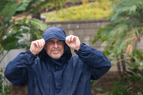 Portrait of mad senior man outside in the rain wearing hood and rain coat