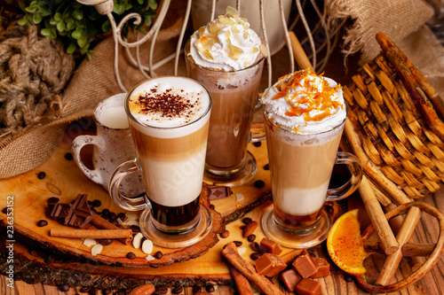Group of three hot layered coffee glasses decorated with whipped cream foam and nuts at xmas wooden table background.