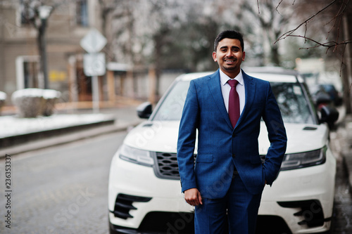 Elegant indian fashionable man model on suit posed at winter day against white business suv car. © AS Photo Family