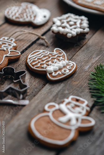 A lot of ginger biscuits in different form on brown wooden table. Decorated with white sweet glaze. Christmas mood, winter morning. Fir branches