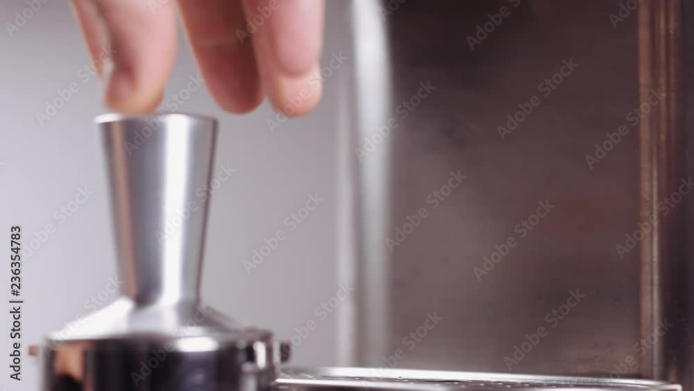 Full process of making coffee. Man hand tamping fresh ground coffee with professional tamper, using filter holder and coffee machine. Barista preparing double espresso and pouring it in glass cup.