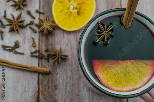 Fototapeta Naklejka Na Ścianę i Meble -  Hot mulled wine drink with lemon, apple, cinnamon, anise and other spices in a glass cup between fir tree branches on wooden cutting board