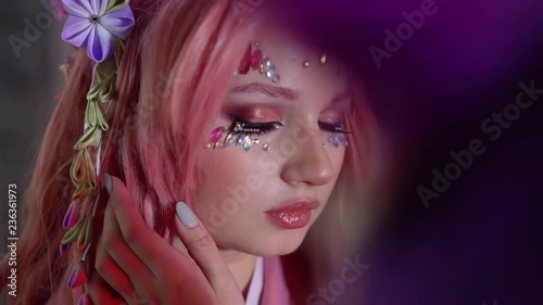 young pretty girl with pink hair and crystals on face is opening eyes and looking at camera