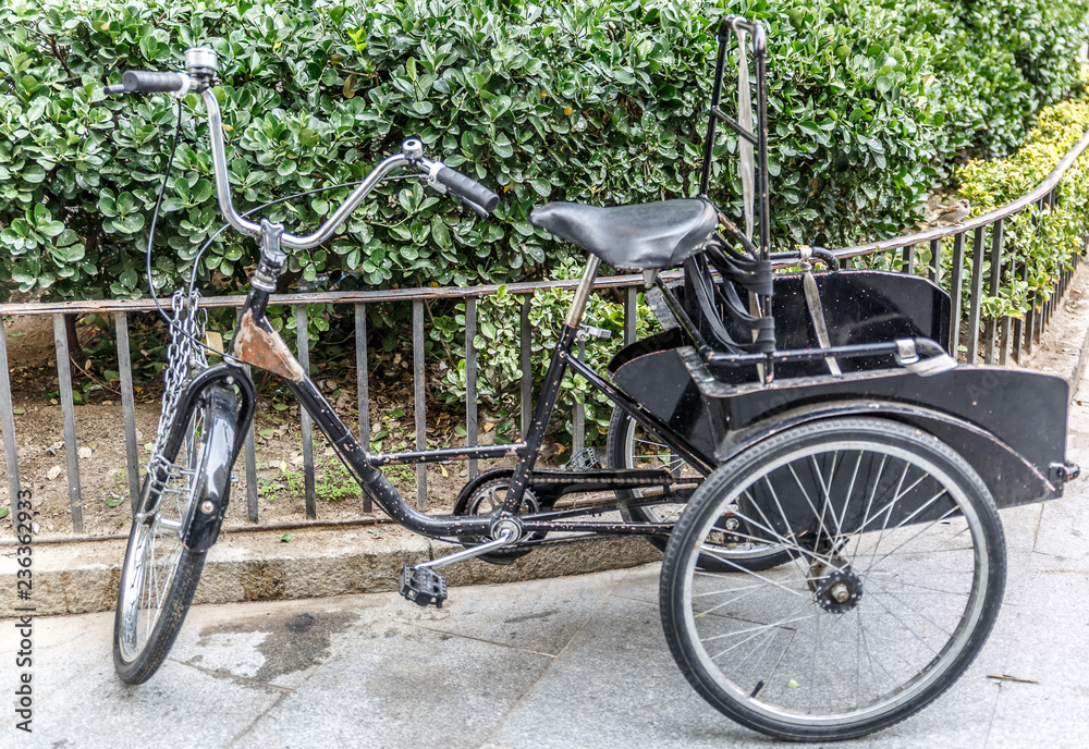 Bicycle with three wheeled tied to a small metal fence Bicycle with three wheeled tied to a small metal fence