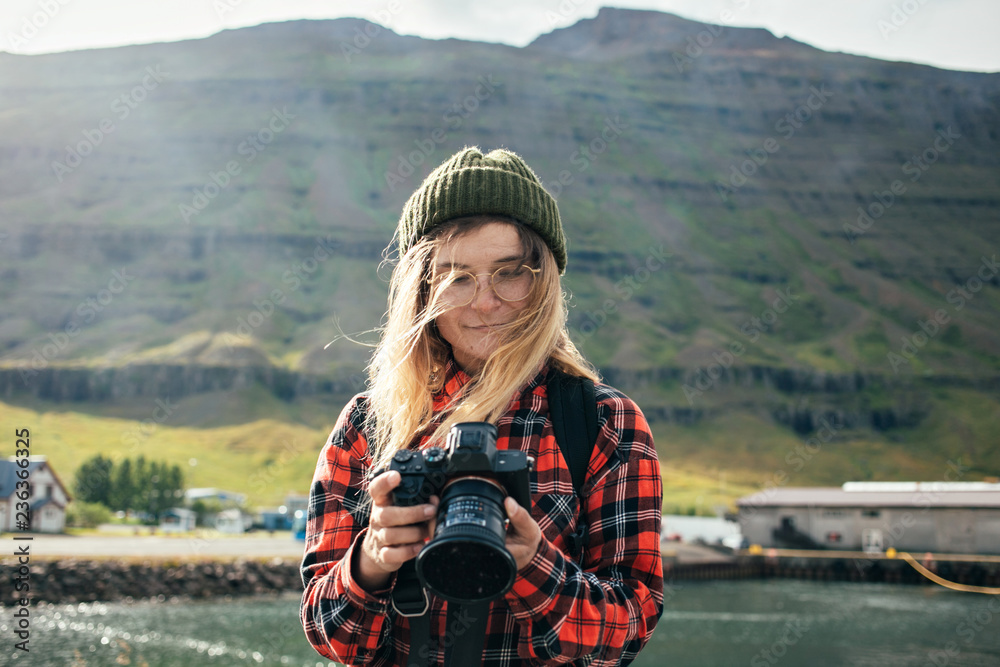 Young fashionable female tourist or photographer looks and inspects photos on digital dslr camera. Influencer or social media blogger creates content for blog on iceland roadtrip Young fashionable female tourist or photographer looks and inspects photos on digital dslr camera. Influencer or social media blogger creates content for blog on iceland roadtrip