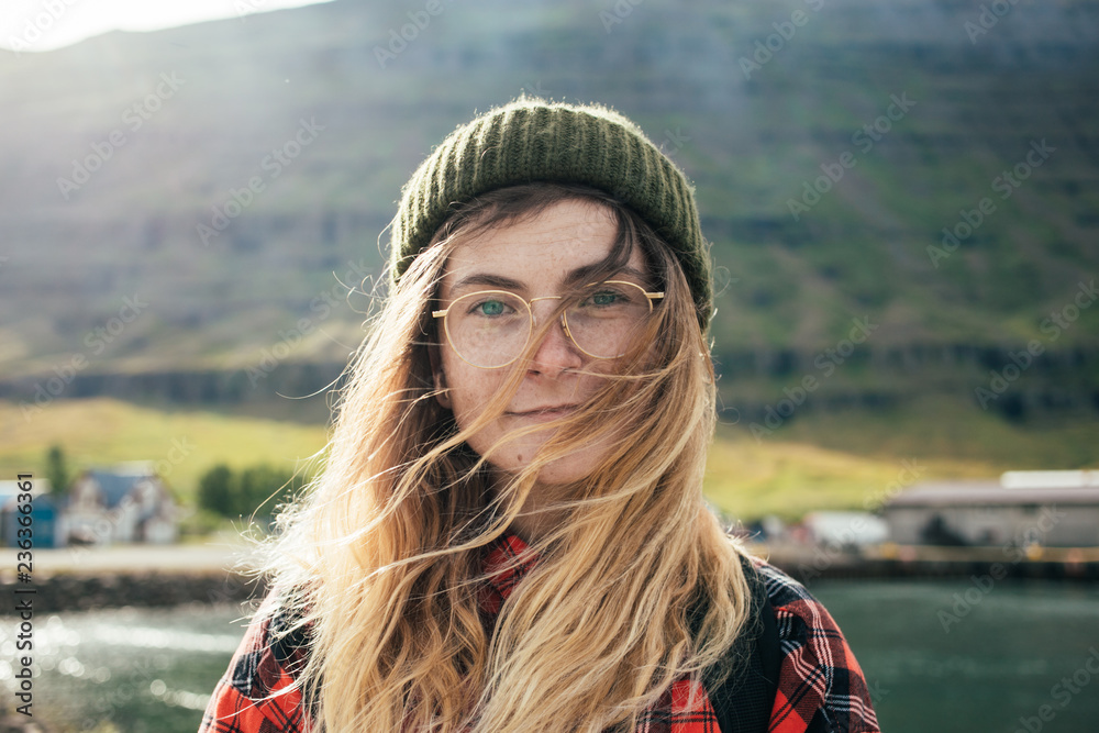 Portrait of young natural beautiful woman or girl with bright blue eyes and blonde  hair in wind, wear green beanie and red hipster shirt, look at camera,  gently smile Stock Photo