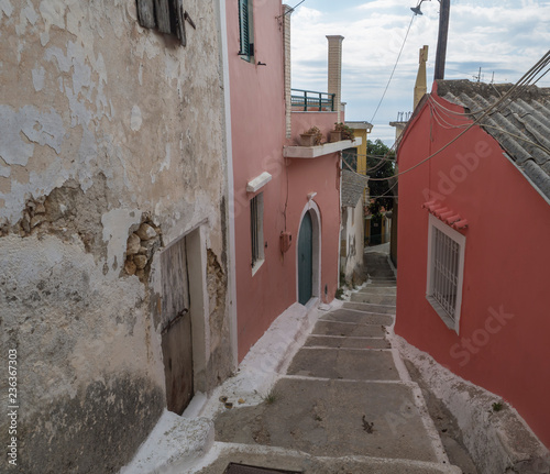 narrow street and stairs with old red houses and green door, vintage look, Corfu Greece