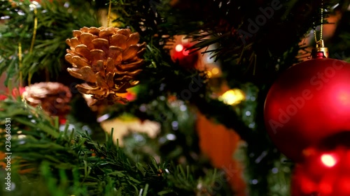 Decorated Christmas tree with red and gold balls and wooden Pinocchio toy. Dolly shot of Christmas holidays celebration. Blurred, sparkling and fairy background with green pine branches and cones.