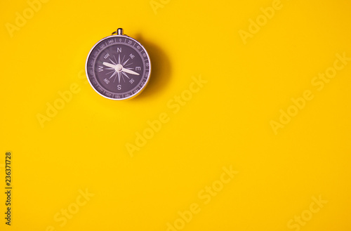Black compass on yellow background, equipment for travel, tourism and business, top view and copy space
