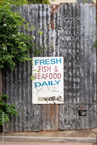 An old, weathered Fresh Fish and Seafood sign in a back lane way