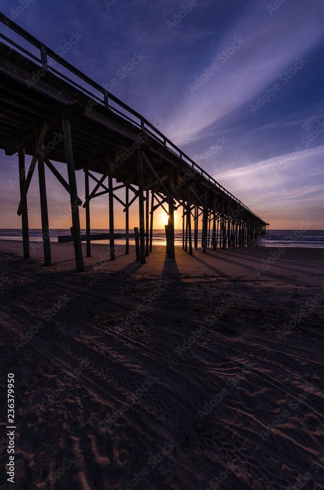 Rays of light at sunset behind a pier at Carolina Beach, North Carolina, USA