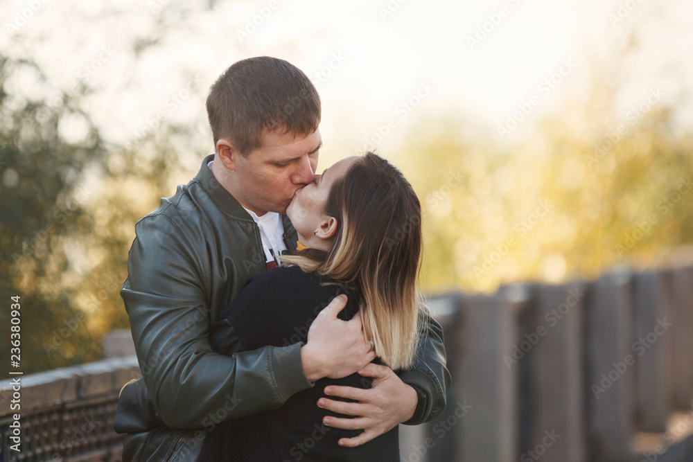 Young couple boy and girl hug and kiss in autumn park. Fall. Young Man and Woman outside. Happy family Concept. Young couple boy and girl hug and kiss in autumn park. Fall. Young Man and Woman outside. Happy family Concept.
