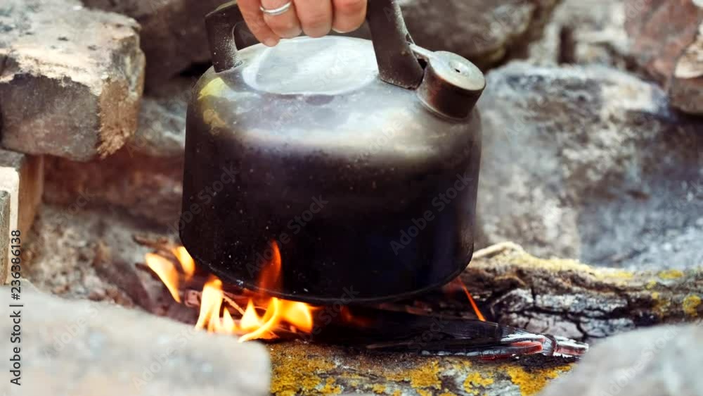 Dolly shot of old metal kettle on camping fire with boiling water. Traveler man hand taking teapot from campfire. Tourist making tea with teakettle in the morning on picnic outdoors in forest. Dolly shot of old metal kettle on camping fire with boiling water. Traveler man hand taking teapot from campfire. Tourist making tea with teakettle in the morning on picnic outdoors in forest.