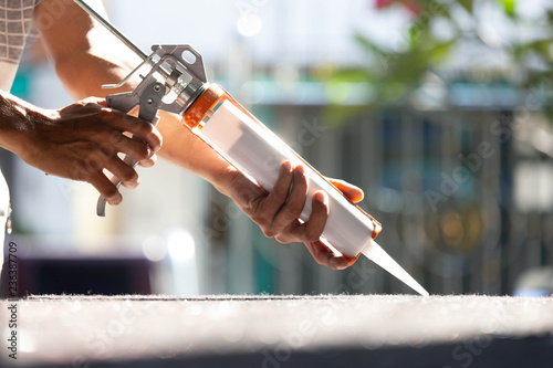 Men's hand uses silicone adhesive with a glue gun to repair worn windows. photo