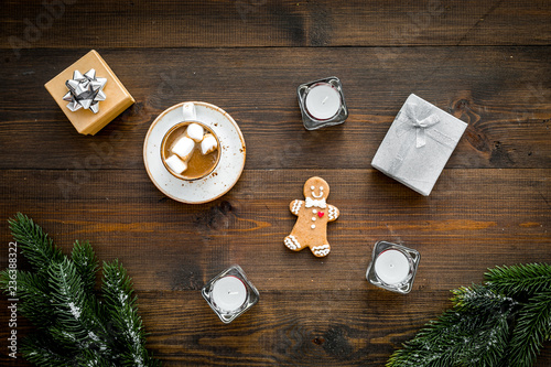 New Year or Christmas concept with hot drink. Cocoa with marshmallow, gift box, gingerbread man, candles, fir branches on dark wooden background top view