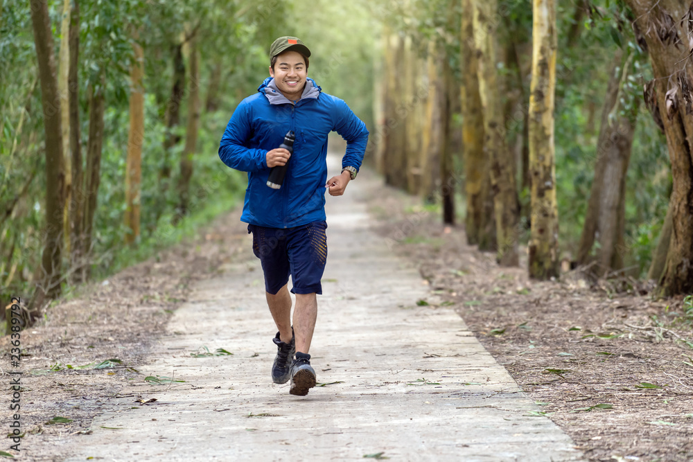 Asian runner in sport suit are running with happiness action in deep forest in evening time, healthy and exercise concept Asian runner in sport suit are running with happiness action in deep forest in evening time, healthy and exercise concept