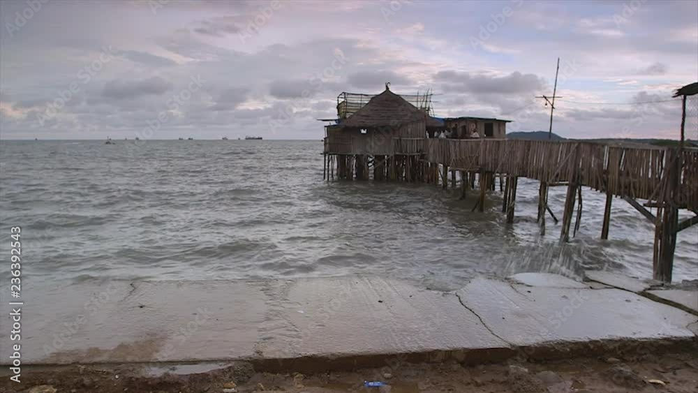Amusing wide still shot, Obama pub, caf�, Conakry, made of a shack, supported by many tilts firmly fixed under light-grey water, hanging wooden bridge, covered sides, rough flat, concrete plaster Amusing wide still shot, Obama pub, caf�, Conakry, made of a shack, supported by many tilts firmly fixed under light-grey water, hanging wooden bridge, covered sides, rough flat, concrete plaster