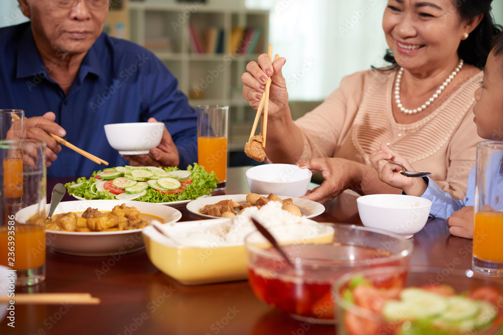 Smiling aged Asian woman enjoying tasty food at family dinner