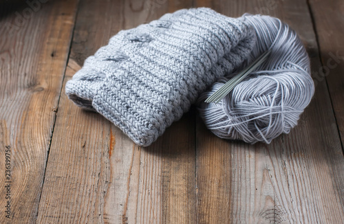 wool grey hat, knitting needles and yarn on wooden background
