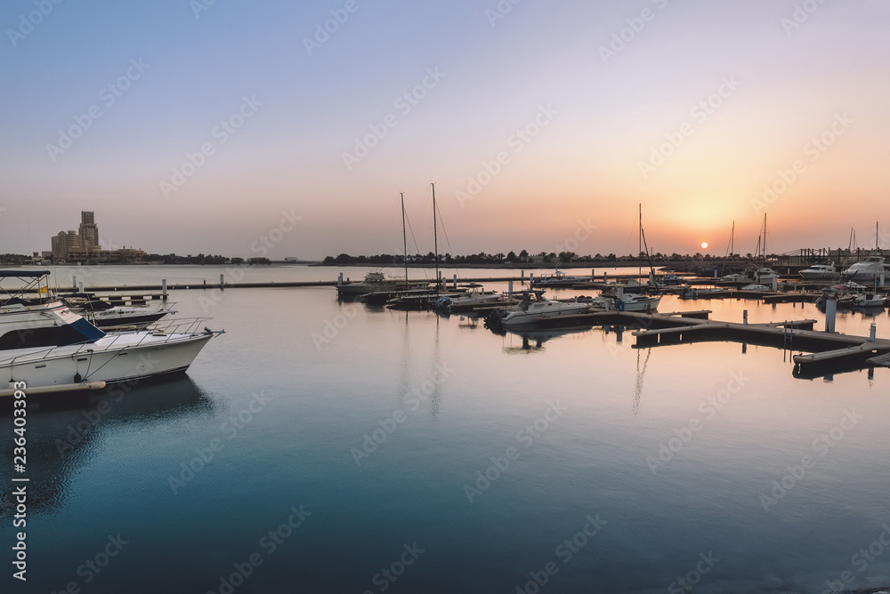 September 12, 2017 - Al Hamra Village in Ras al Khaimah, United Arab Emirates. Marina, pier and parked yachts. Arabian harbor with sailboats reflected in water by sunset.
