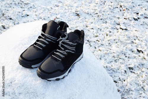 Pair of black new man hightop sneakers or boots with laces on stone covered by snow on snowy field background with copy space for text.