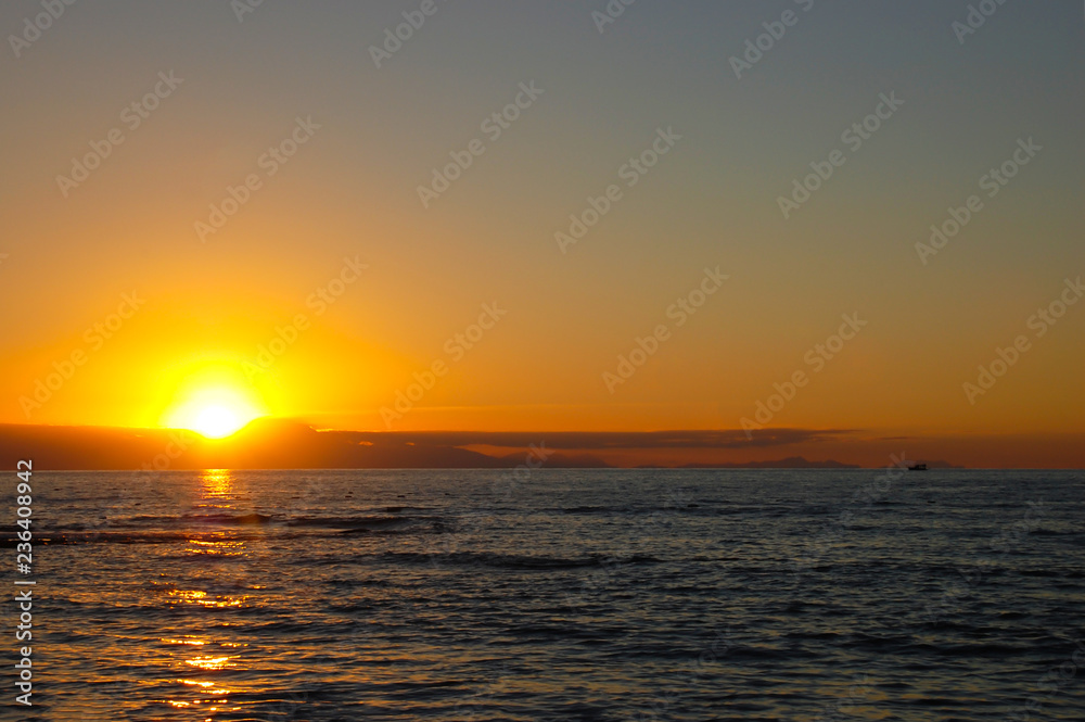 Beautiful sunset over the sea with an endless horizon and a lonely boat in the distance