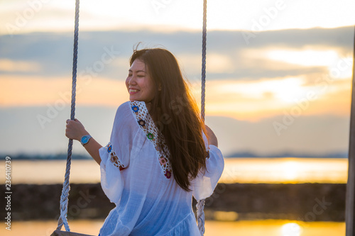 young beautiful and happy Asian Korean woman enjoying summer holidays trip at beach resort smiling cheerful on swing having fun feeling free and relaxed photo