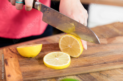 Close up of woman slicing lemon on cutting board.