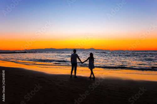 A man and a woman by the sea are watching the sunset.