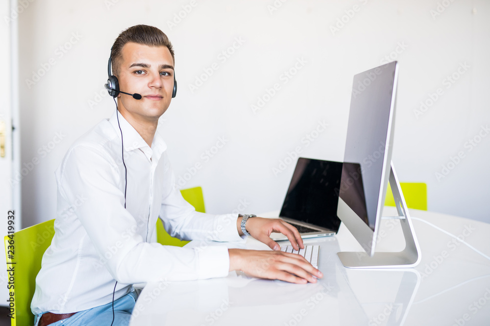 Portrait of a smiling young handsome man in formalwear with headset using computer in a office Portrait of a smiling young handsome man in formalwear with headset using computer in a office