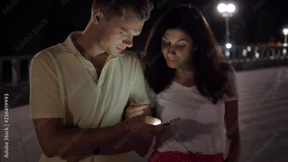 Happy Couple In The Evening On The Street Watching Together In The Smartphone Happy Couple In The Evening On The Street Watching Together In The Smartphone