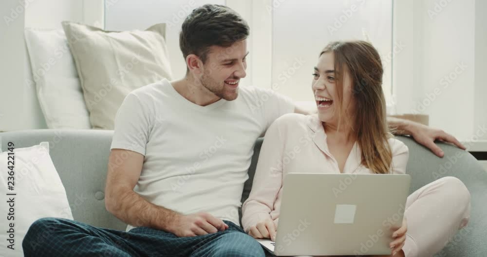 In the pajamas a couple in the morning sitting on the sofa and watching something on the notebook amazing cozy style. In the pajamas a couple in the morning sitting on the sofa and watching something on the notebook amazing cozy style.