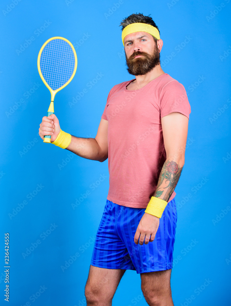 Tennis player retro fashion. Athlete hold tennis racket in hand on blue  background. Tennis sport and entertainment. Tennis club concept. Man  bearded hipster wear old school sport outfit with bandages Stock Photo