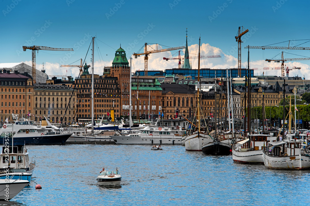 Stockholm harbor, sailboats, yachts and ships moored to a embankment in a city center with construction cranes and cityscape on a background. Sweden