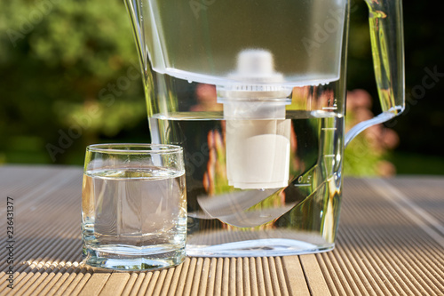 Plastic water filter pitcher and a clean glass of a clear water close up on the summer garden background