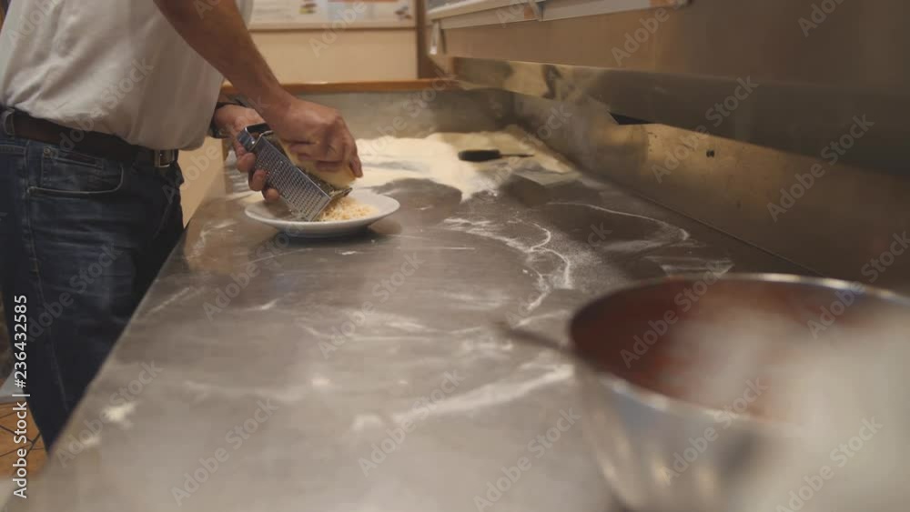 Man grates hard cheese with grater. Chef makes a filling on professional kitchen Man grates hard cheese with grater. Chef makes a filling on professional kitchen