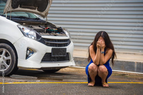 worried woman in stress stranded on roadside with car engine failure having mechanic problem needing repair service and assistance squating on street upset © TheVisualsYouNeed