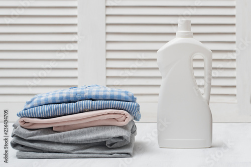 Stack of folded clothes and detergent bottle. White background