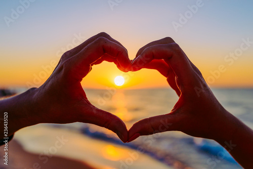 hands forming a heart shape with sunset silhouette