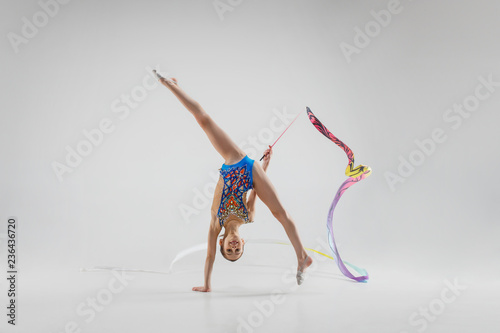 Fotografie The portrait of beautiful young brunette woman gymnast training calilisthenics exercise with blue ribbon on white studio background