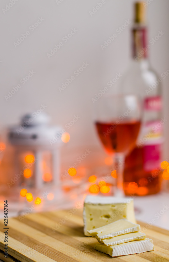 Slices of camembert or brie cheese on the white table with a bottle and a glass of red wine on the blurred background with bokeh. Concept of celebration. Delicatessen 