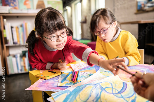 Girl having Down syndrome taking colorful marker from her teacher
