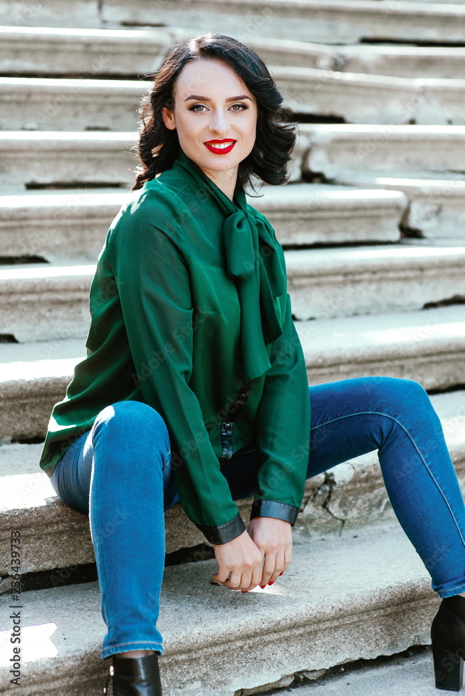 portrait of stylish modern brunette woman in green blouse sitting on tha stairs